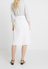 Vit knälång A-linjeformad kjol i linne med en jämn textur, tillsammans med en ljusgrå randig skjorta med knappar och bruna sandaler.