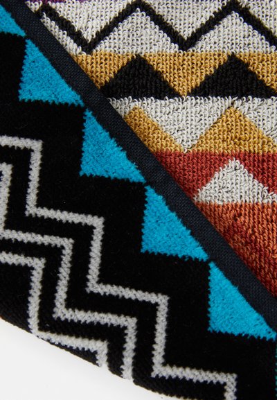 Geometric patterned rug featuring multicolored zigzag and triangle designs in black, blue, gold, and white, with a textured surface.