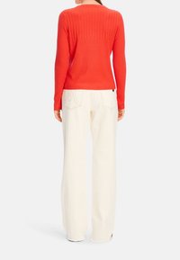 Pull rouge côtelé à manches longues associé à un pantalon blanc à jambes larges, présentant des détails de coutures visibles et une coupe régulière.