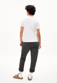 Witte t-shirt met korte mouwen en een relaxte pasvorm, gecombineerd met donkergrijze joggingbroek en bruine sandalen, gezien vanuit de achterkant.