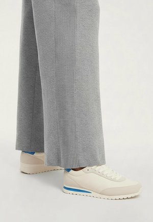 Pantaloni a gamba larga grigio chiaro con dettaglio a costine verticali, abbinati a sneakers color crema con striscia accentuata blu e suola testurizzata.