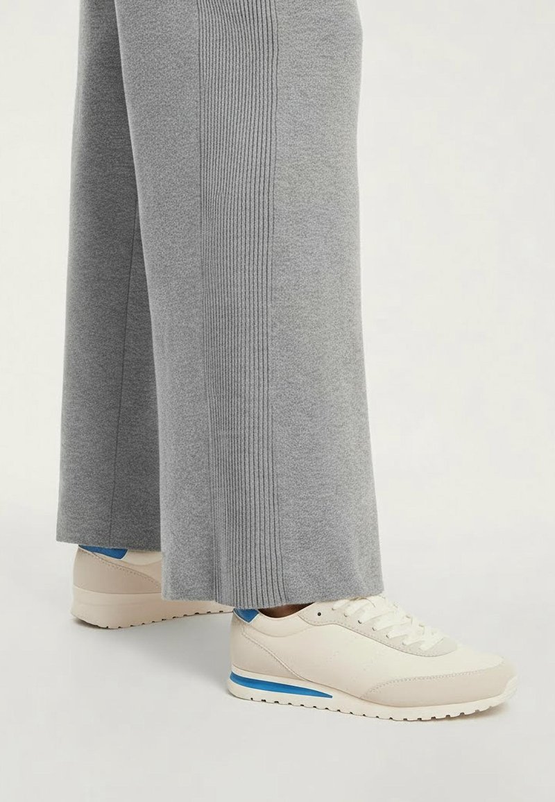 Svetlosivé široké nohavice s vertikálnym rebrovaním, v kombinácii s krémovými teniskami s modrým pruhom a textúrovanou podrážkou.