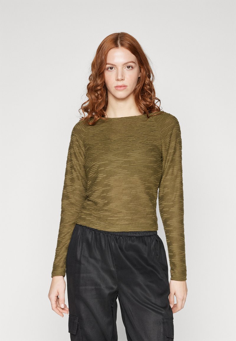 Top lung cu mânecă lungă, texturat, de culoare verde măsliniu, cu un decolteu larg, asociat cu pantaloni cargo negri, cu talie elastică, prezentând o croială relaxată.