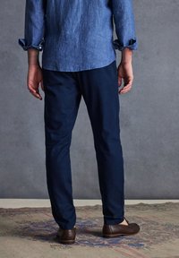 Pantaloni slim-fit blu navy realizzati in un tessuto leggero e morbido, abbinati a scarpe marroni. Maniche di una camicia blu a vista, con risvolto.