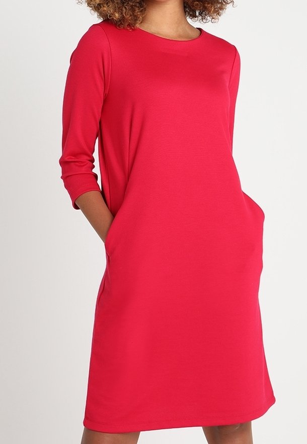 Robe rouge, longueur genou en tissu doux avec des manches trois-quarts et des poches latérales. Col rond simple et coupe décontractée.