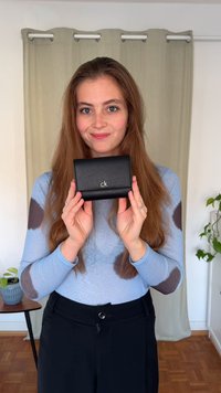 Juodas odinis piniginė su sidabriniu „ck“ logotipu. Kompaktiškas, stačiakampio formos dizainas su lygiu paviršiumi ir sulankstomu užsegimu.