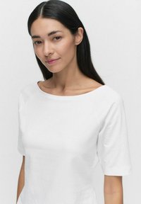 Vit t-shirt med kort ärm och vid, rund halsringning, tillverkad av ett mjukt bomullstyg. Enkelt utformad med minimala sömdetaljer.