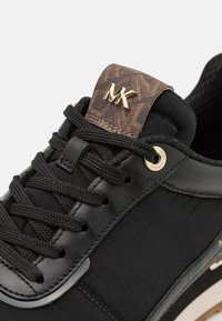 Sneaker nera con un mix di pelle liscia e tessuto testurizzato, dettagli in hardware dorato e un tallone in tessuto marrone scuro a fantasia con logo.