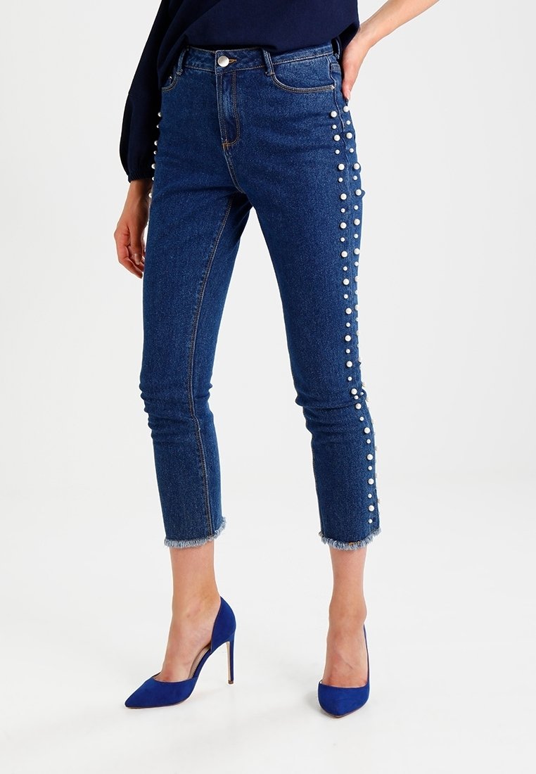Jeans i denim med medelhög midja, prydda med pärldekorationer längs sidan och en fransad fåll. Färgen är mörkblå.