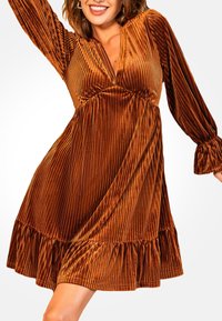 Vestido de terciopelo de color naranja quemado, con mangas largas, escote en V y dobladillo acampanado. Presenta una cintura fruncida y puños con volantes.