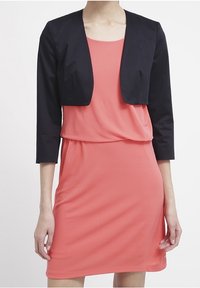 Korallklänning i kombination med en kort svart blazer. Klänningen har en löst sittande passform, medan blazern har trekvartsärmar och en slät yta.