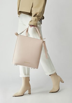 Sac à main en cuir rose clair de forme carrée avec deux poignées supérieures et une bandoulière réglable. Texture lisse, design minimaliste, avec logo sur le devant.