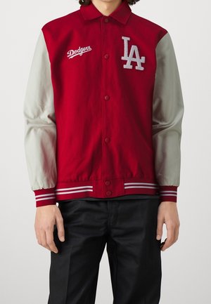 Person trägt eine rote Collegejacke mit grauen Ärmeln, weißem "Dodgers" Schriftzug auf der linken Brust und grauem "LA" Logo auf der rechten Brust.
