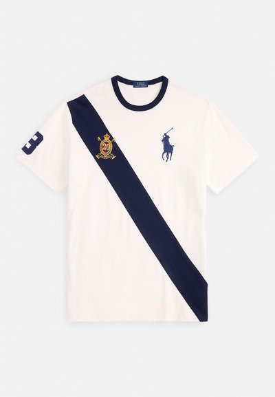 Βαμβακερό T-shirt σε λευκό χρώμα με μια γαλάζια λοξή ρίγα. Διαθέτει λογότυπο παίκτη πόλο, έμβλημα κορώνας και τον αριθμό "3" στο μανίκι.