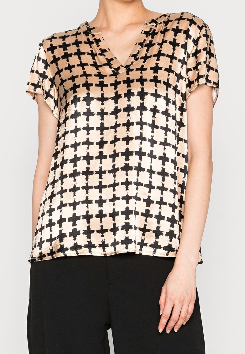 Kortärmad blus med V-ringning i ett kräm- och svart geometriskt mönster, tillverkad av ett glatt tyg med lös passform och sidoflikar.