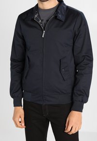 Marinblå bomberjacka i ett slätt material med dragkedja, sidofickor, ribbade muddar och fåll samt ett rutigt foder på insidan.