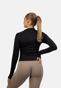 Crna dugorukava uska majica od rastezljivog materijala, s visokim ovratnikom i bešavnom dizajnom, u kombinaciji s svijetlim bež tajicama.