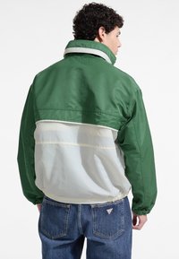 Zielona i off-white wiatrówka z wysokim kołnierzem, elastycznymi mankietami i ściągaczem u dołu. Gładki, lekki materiał.