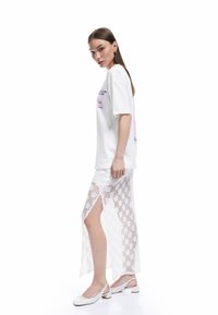 Vit oversized t-shirt med färggrafisk tryck, i kombination med en genomskinlig vit spetskjol med sidoklyv och blommönster. Vita ballerinas.