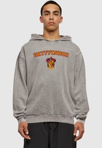 Šedá mikina s kapucí s logem "GRYFFINDOR" v oranžové barvě nad barevným erbem. Měkká textura, uvolněný střih a žebrované manžety.