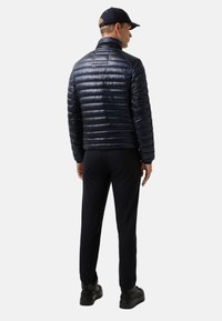 Námornická péřová bunda s vysokým límcem, horizontálně prošívanou strukturou a lesklým povrchem, oblečená s tmavými kalhotami a černými botami.