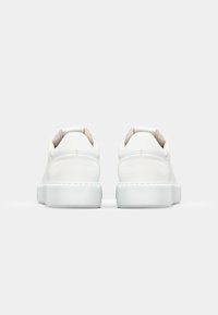 White leather sneakers with a smooth finish, rounded shape, padded collar, and a flat, rubber sole. Minimalist design without patterns.