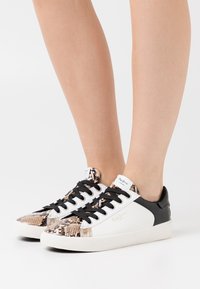 Sneakers con una toma in stampa rettile testurizzata nei toni del marrone e del nero, con un lato in pelle bianca e dettagli neri. Lacci neri.