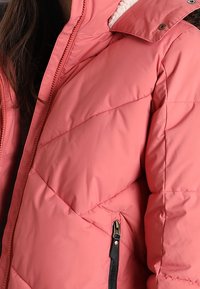 Veste matelassée rose avec un col montant, dotée d'une poche zippée et d'une doublure en peluche texturée. Légère, avec des motifs de couture diagonaux.