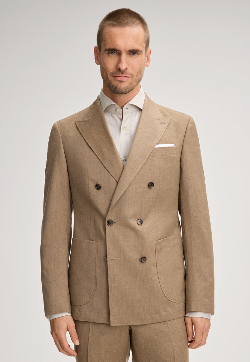 Beige Doppelreiher-Sakko mit zwei vorderen Taschen, eingeknoteten Revers und dunklen Knöpfen. Getragen über einem hellen Hemd. Glatte Textur.