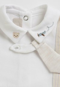 Chemise en coton blanc avec un col, ornée de motifs brodés d'un ours et de bobines de fil. Comprend une cravate beige à motif rayé.