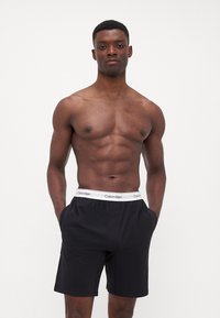 Zwarte Calvin Klein boxershorts met een witte, gebrandmerkte tailleband, met een relaxte pasvorm en twee zijzakken.