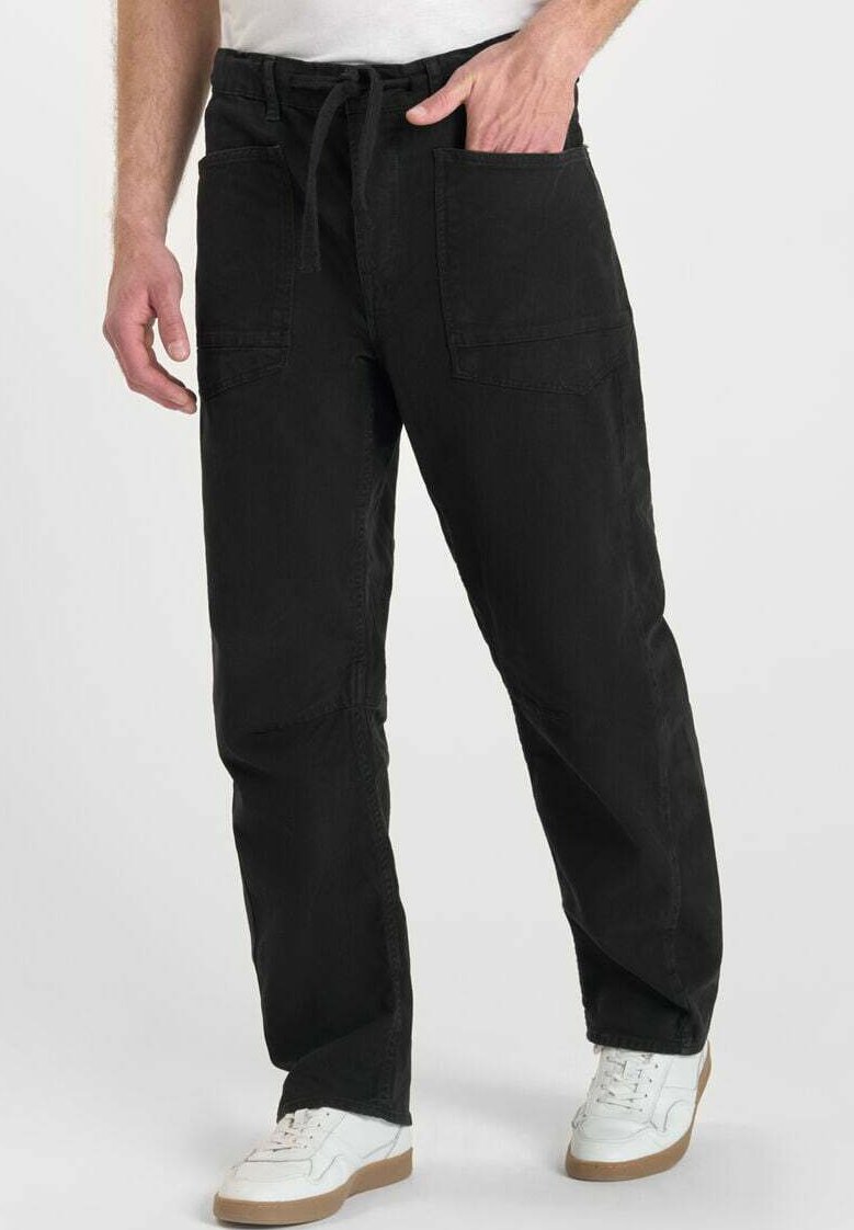 Zwarte cargobroek van katoen, met een trekkoord in de taille, twee grote voorkruiden en een relaxte pasvorm. Draagt met witte sneakers.