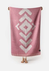 Manta rectangular de color rosa con un patrón geométrico blanco. Fabricada en tela suave, cuenta con bordes con flecos. El patrón incluye diamantes y flechas.