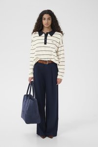 Polo de manga larga a rayas crema con cuello oscuro, combinado con pantalones anchos azul marino y un bolso tote de ante azul. Cinturón de cuero marrón que acentúa la cintura.