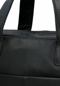 Schwarze Lederhandtasche mit zwei stabilen Griffen, ausgestattet mit einer glatten Oberfläche und eingeprägtem Logo. Minimalistisches Design ohne zusätzliche Beschläge oder Akzente.
