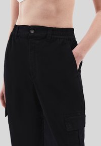 Černé cargo kalhoty s elastickým pasem a knoflíkovým zapínáním. Mají boční kapsy a volný střih, vyrobené z hladké, odolné tkaniny.