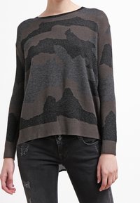 Grau strukturierter Pullover mit einem Camouflage-Muster in verschiedenen Schwarz- und Brauntönen. Verfügt über einen weit ausgeschnittenen Halsausschnitt und einen gerippten Saum.
