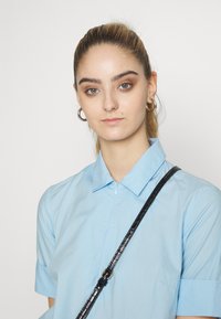 Camisa azul clara com colarinho e mangas curtas, feita de um tecido suave, combinada com uma faixa preta texturizada. Design simples, sem padrões.