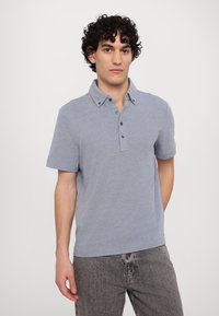 Light blue short-sleeve polo shirt with a collar, three-button placket, and a textured fabric. Paired with dark gray jeans.
