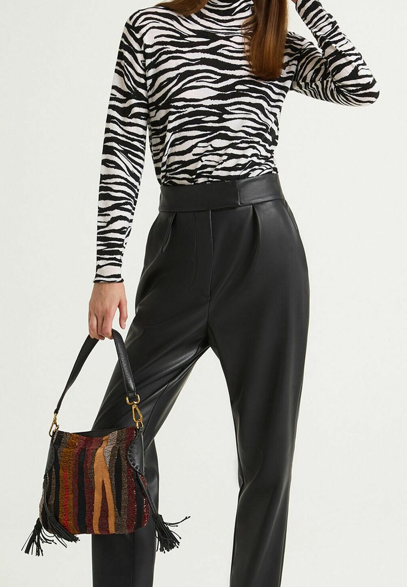 Dolcevita a righe zebrate in bianco e nero abbinato a pantaloni in pelle neri a vita alta. Tiene in mano una borsa multicolore con motivi e nappine.