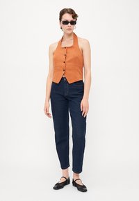 Různofarebný oranžový halter top s knoflíky a dvěma předními kapsami, spojený s tmavě modrými zúženými džíny a černými plochými botami. Hladká, strukturovaná tkanina.