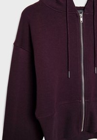 Sweat à capuche zippé de couleur violet foncé avec cordons, poignets et ourlet côtelés, montré de l'épaule à la taille.