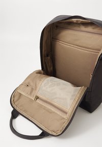 Sac à dos noir avec un intérieur beige. Comprend une poche zippée en maille, des compartiments supplémentaires et une texture douce. Fermeture zippée.
