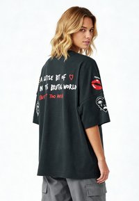 Pārmērīgi liela melna kokvilnas T-kreklu ar krāsainām uzrakstiem un dizainiem. Piedurkņu apakšā ir lūpu un skumju seju grafikas. Mīksta tekstūra, brīvi pieguļošs stils.