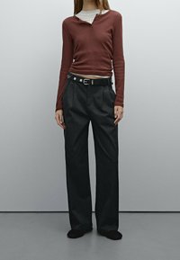 Langsleeve roestkleurig gebreid shirt bovenop een wit shirt, gecombineerd met hoge, wijde donkere broek, accenten van een zwarte riem met zilveren hardware.