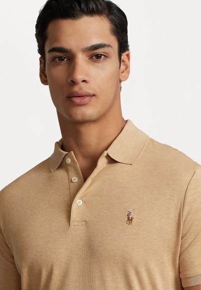 Beige polo särk koos krae ja kahe nööbiga, millel on väike, tikitud logo polo mängijast. Pehme kudumise tekstuur.