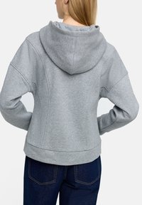 Szara bluzka z kapturem o luźnym kroju, charakteryzująca się miękką teksturą, ściągaczami na rękawach i lekko zaokrąglonym dołem. Widoczne detale szwów.