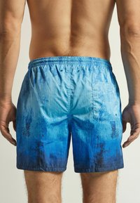 Bañador en degradado azul, con una cinturilla elástica, un bolsillo trasero y un tejido suave y ligero con un acabado ligeramente texturizado.