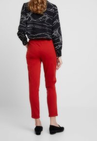 Rode slim-fit broek met een gladde textuur, voorzien van een omgeslagen zoom. Gecombineerd met een zwart met patroon blouse, geaccentueerd door een simpele zwarte schoen.