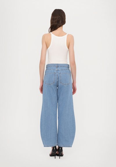 Wide-leg light blue denim jeans with a high waist, two back pockets, and a relaxed fit. Paired with a white tank top and black heels.